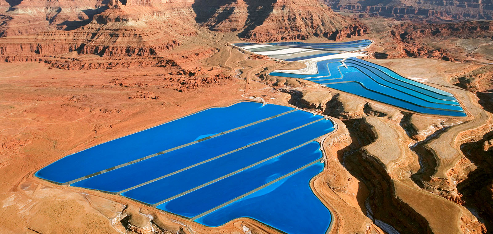  An aerial view of a rocky red desert is sharply contrasted by two royal blue, brim-filled water treatment reservoirs.