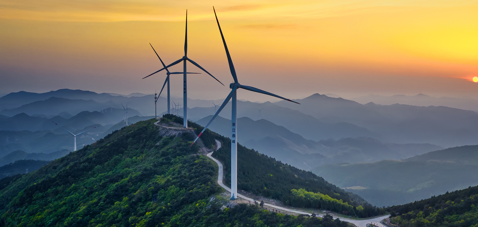 Wind turbines snake across a mountaintop in the Chinese province of Jinhua, while the sun rises in the distance. 