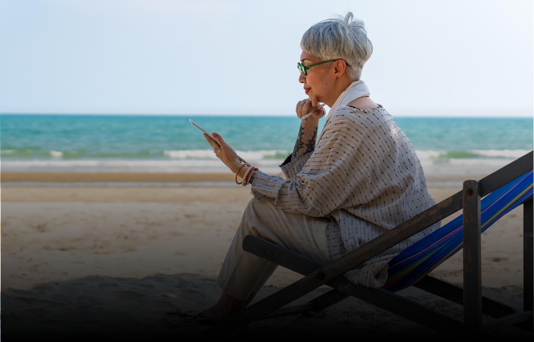 Retired woman on a beach looking at her iPad.