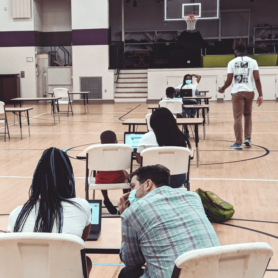 Teachers and students working in a gym, socially distanced with masks on