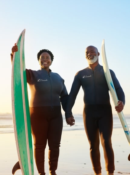 Older couple walking on beach with surf boards