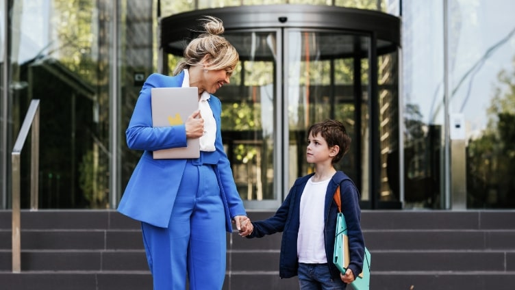 Working mother in blue work suit holding hand of young boy outside office building