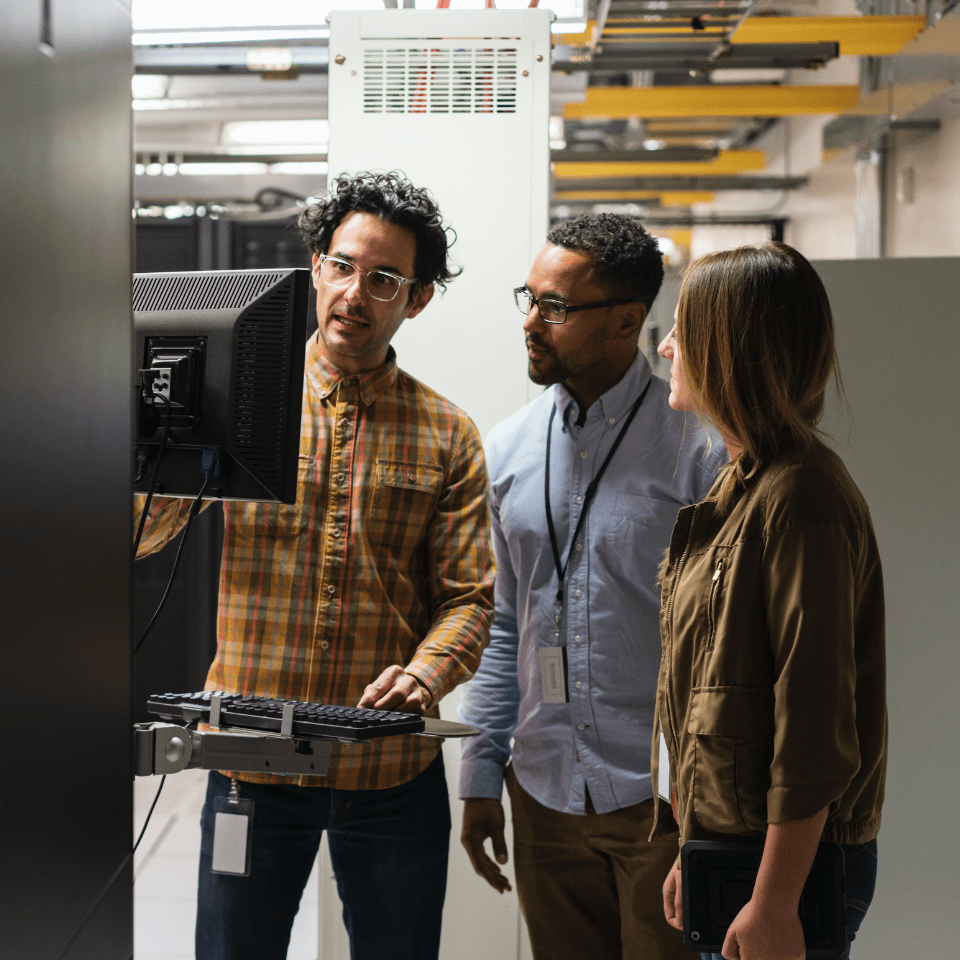 Three technology professionals looking at a computer in a data server room 