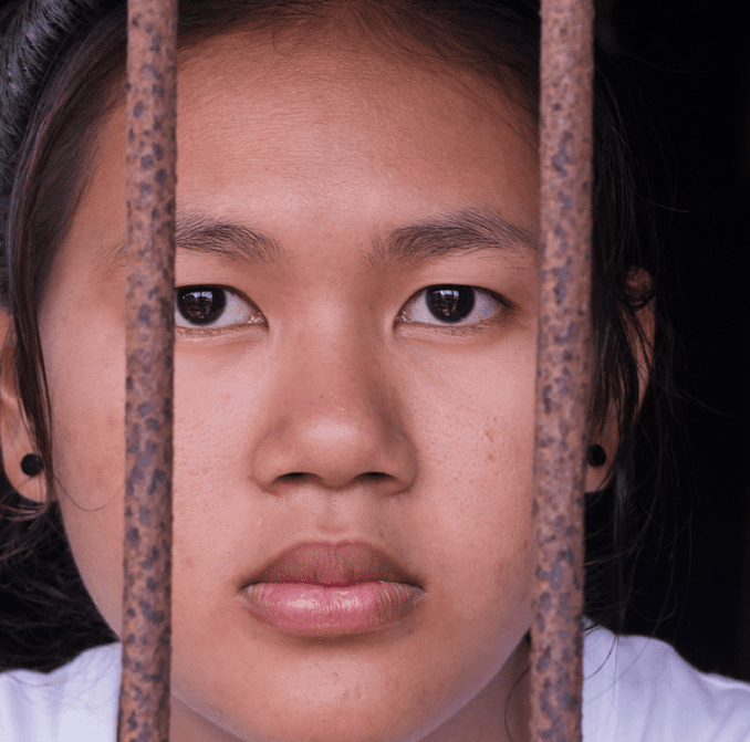 Young girl of Asian decent peering out from behind iron bars