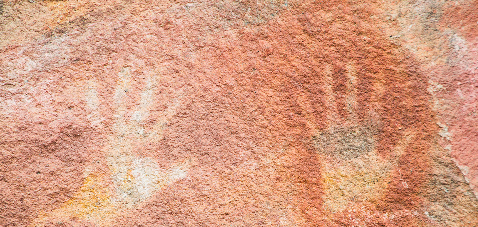 Two large handprints sprawl across the wall of a bright red cave, blending with the color and texture of the rock.