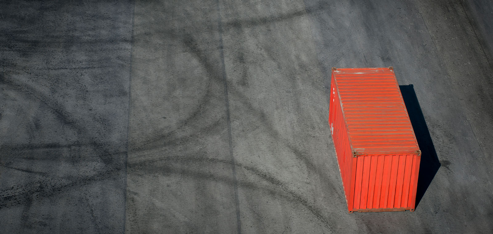 A lone red cargo container sits in a large, vacant shipping storage area.