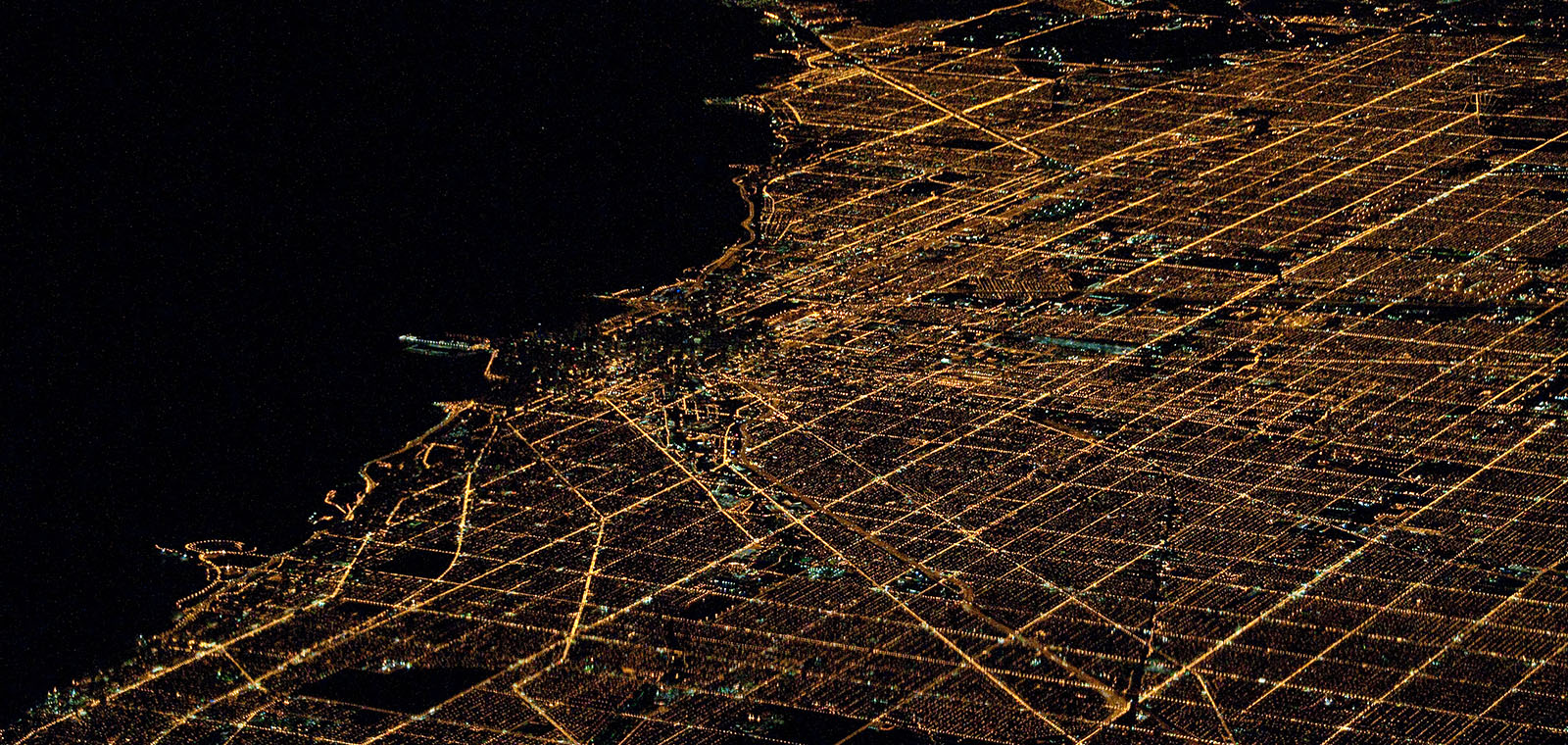 The glowing lights of a large city create web-like patterns in the dark night.
