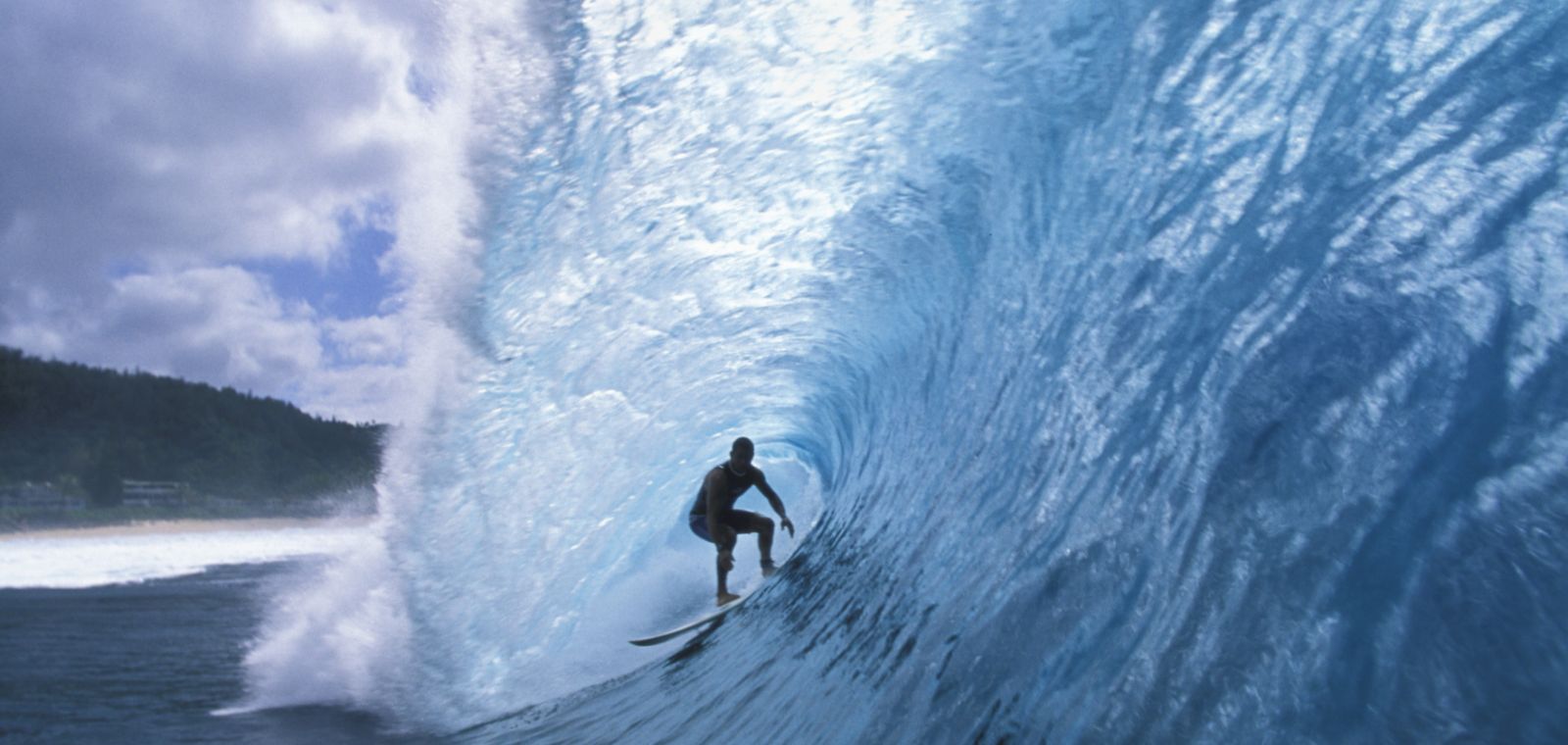 A surfer on a board under a blue ocean wave cresting over him