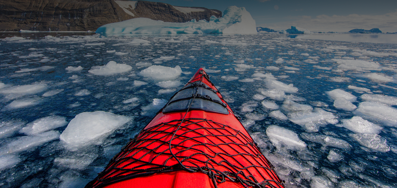 Forward view from the seat of a red kayak navigating an arctic sea full of floating chunks of ice.