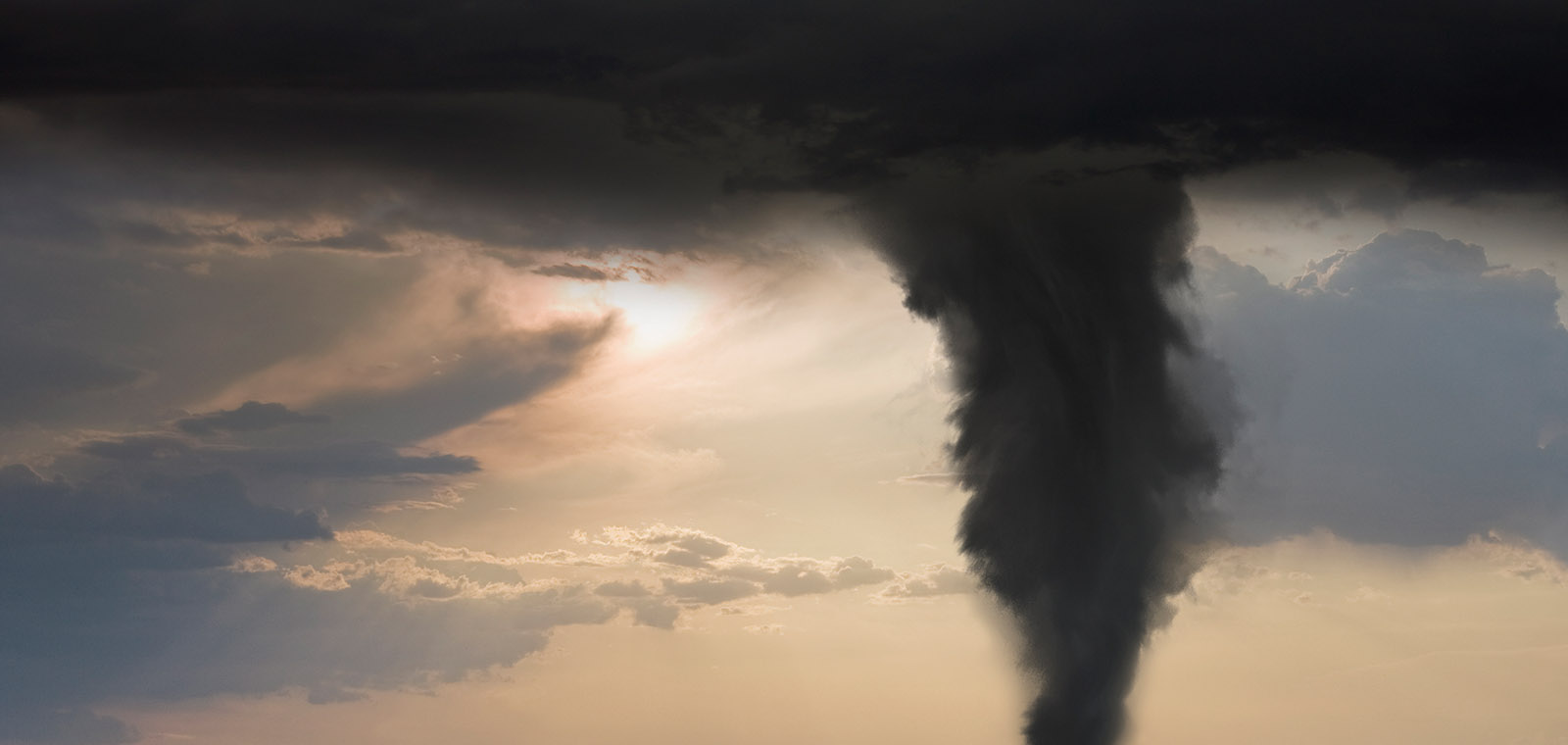 The menacing shape of an oncoming tornado dominates the skyline over a bleak landscape.